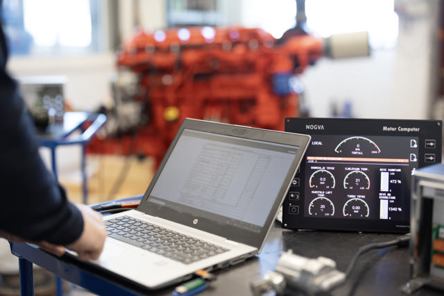 Datamaskin på en arbeidsbenk som programmerer Nogva Motor Computer, rød Scania motor i bakgrunnen
